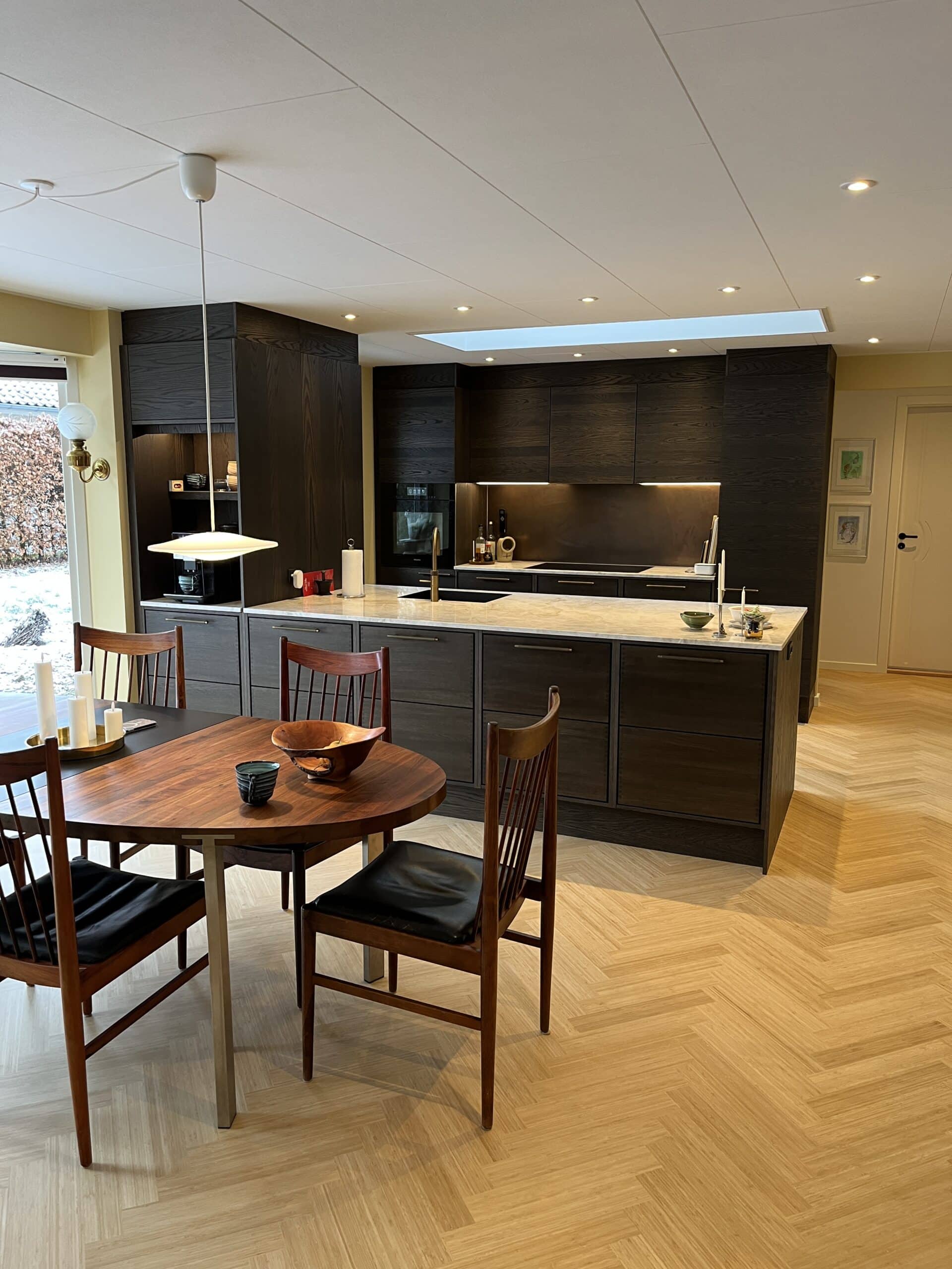 Ny renoveret køkken alrum med nyt ovenlysvindue, sildebensparketgulv og moderne mørkt køkken med stor køkkenø